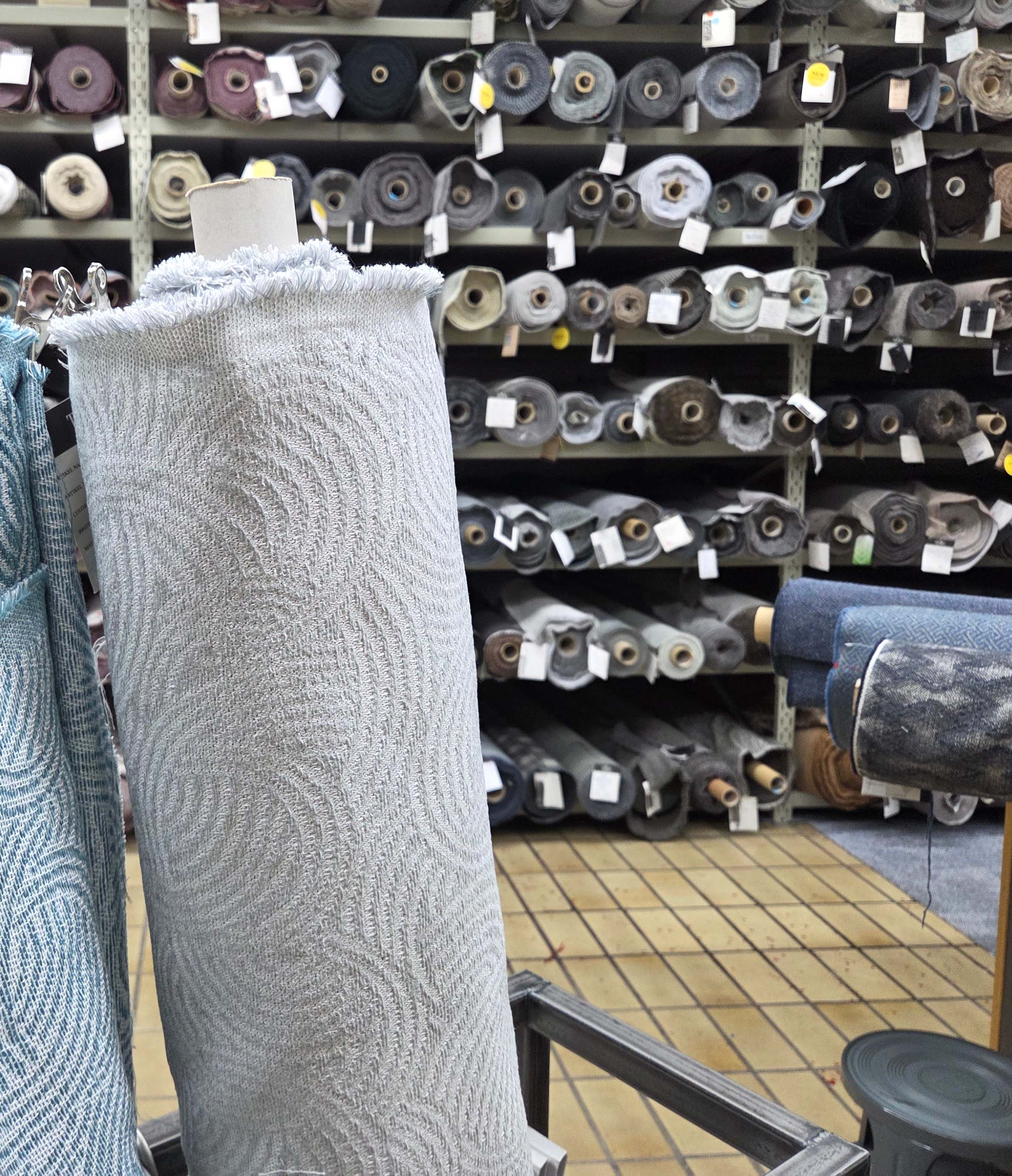 High-quality designer fabric rolls in a deadstock warehouse, two gray rolls in the foreground.