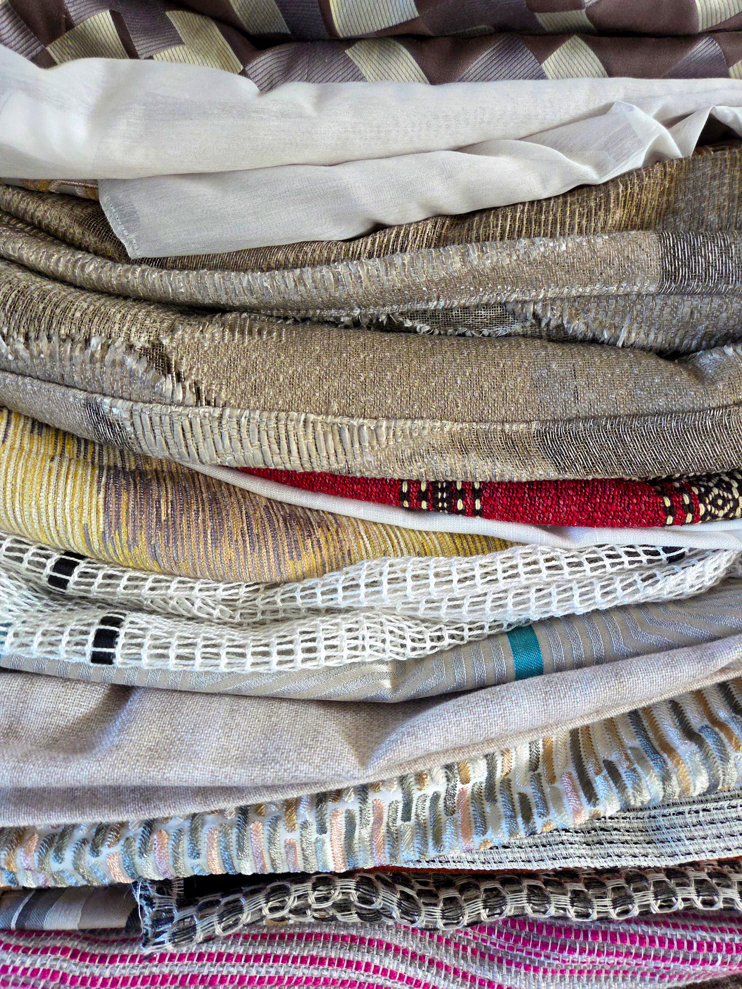 Bunt gemixte, locker gestapelte Gardinenstoffe in verschiedenen Farben aus Deadstock-Beständen.